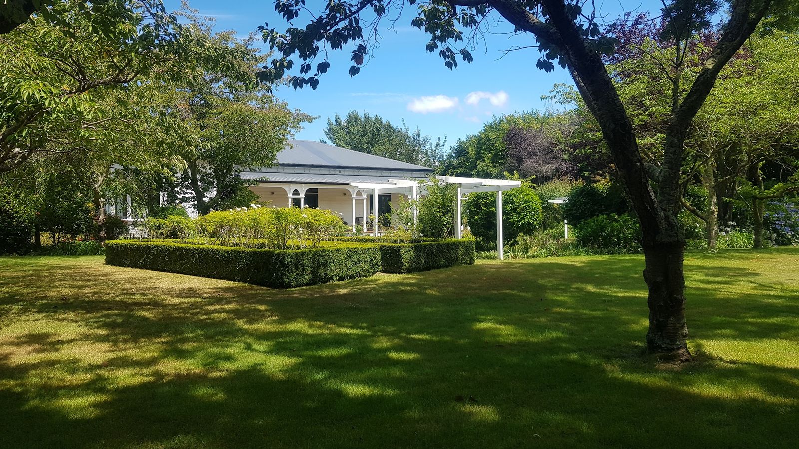 Mown lawn and clipped box hedge in front of a villa with a veranda